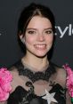 Anya Taylor-Joy smiles brightly, showcasing her unique style with bold fashion details and elegant makeup at a recent event.