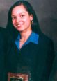 Young woman smiling in a blue shirt and black blazer, holding an award plaque, exuding confidence and professionalism.