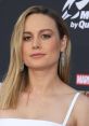 Brie Larson at a red carpet event, wearing elegant earrings and a stylish white dress, showcasing her sophisticated look.