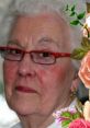 Elderly woman with short white hair and red glasses, framed by floral decorations, exuding warmth and wisdom.