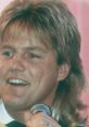 Dieter Bohlen in the early years, smiling with a microphone, showcasing his iconic hairstyle and charming stage presence.