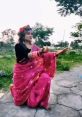 Woman in a pink saree dancing gracefully outdoors, showcasing traditional culture and vibrant attire against a lush backdrop.