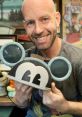 Bret Iwan, voice of Mickey Mouse, smiles while holding Mickey-themed headphones labeled "On Air.