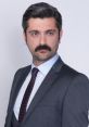 Oktay Gurcay in a tailored gray suit, showcasing his distinctive mustache and confident expression, perfect for promotional use.