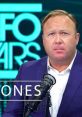 Alex Jones on-air at InfoWars, discussing controversial topics with intense focus, wearing a blue suit and microphone setup.