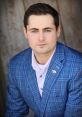 Professional portrait of Jack Murphy in a blue plaid suit, showcasing confidence and style with an American flag pin.