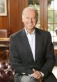 Joe Biden smiling in a dark suit, seated in an elegant room with wooden decor, showcasing a confident and approachable demeanor.