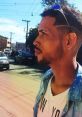 Man in stylish attire stands on a city street, showcasing cool sunglasses and a modern hairstyle, exuding urban flair.