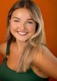 Cheerful portrait of Olivia Goodman with a bright smile, wearing a green top against a vibrant orange background.