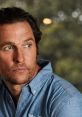 Matthew McConaughey gazes thoughtfully, showcasing his rugged charm in a stylish denim shirt against a blurred background.