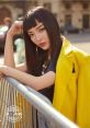 Vava showcases a striking fashion look with a yellow jacket and sleek hairstyle in an urban setting, exuding confidence.