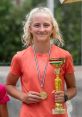 Greta Buda proudly holding a trophy and medal, celebrating her victory at a tennis tournament.