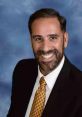 Professional portrait of Luiz Fernando Lopes, smiling in a suit with a patterned tie against a blue background.