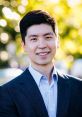 Portrait of Yang Hoon Cho, smiling confidently in a suit, with a bright, blurred background of nature.