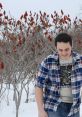 Gianni Matragrano enjoying winter outdoors, wearing a plaid shirt and surrounded by snow and vibrant red sumac.