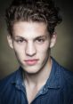 Young man with curly hair and piercing eyes, wearing a denim shirt, exuding confidence and charisma. Perfect for modeling.