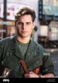 Young man in military uniform with patches, exuding confidence and charisma, likely portraying a character's role.