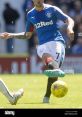 Rangers player in blue jersey kicking a soccer ball on the field, showcasing skill and athleticism during a match.