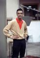 Stylish young man in a beige cardigan and red shirt stands confidently in a recording studio, capturing a vintage vibe.