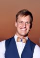 Smiling young man in a navy vest and unique wooden bow tie, capturing a warm sunset backdrop.