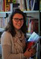 Élise Desbois smiling while holding a book in a cozy library setting, surrounded by shelves of various books.