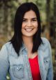 Smiling woman in a denim shirt and red top, surrounded by greenery, captures a vibrant outdoor personality. Gabrielle Gaudet.