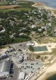 Aerial view of the Dennis Club area, featuring residences, a tennis court, and a marina with boats. Ideal for coastal recreation.