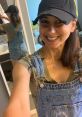 Smiling woman in denim overalls and a black cap, showcasing confidence and style in a bright, modern bathroom setting.