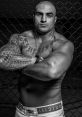 Fernando Rodrigues, muscular MMA fighter, showcasing tattoos and fierce expression in an octagonal cage setting.