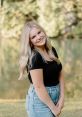 Lily Horridge smiles confidently outdoors by a serene lake, showcasing a stylish black top and high-waisted jeans.