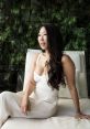 Angie Wang sitting elegantly in a white dress, surrounded by lush greenery, showcasing her stylish and confident demeanor.