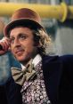 Gene Wilder as Willy Wonka, wearing a brown top hat and floral attire, exudes charisma and whimsy in the chocolate factory.