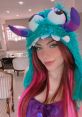 Miih Ares Azevedo poses with vibrant pink hair and a playful monster hat, showcasing her fun personality and style.