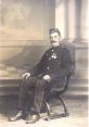 William MacKay, in a formal uniform with medals, seated in a vintage chair, showcasing early 20th-century attire.