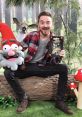 Alex Hirsch joyfully presents "Gravity Falls" book, featuring characters and whimsical props in a forest setting.