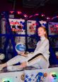 Tess B poses with a basketball at an arcade, showcasing her sporty style and confidence among vibrant game machines.