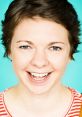 Smiling young woman with short hair, wearing a striped shirt, against a teal background, radiating positivity and charm.