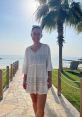 Laura O'Shaughnessy enjoying a sunny beach day in a white dress with palm trees and ocean in the background.