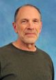 Maxwell Bachenheimer smiling in a casual green shirt against a blue background, showcasing his approachable demeanor.