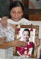 Woman holding a framed portrait of Geetika Sharma, adorned with flower garlands, showcasing remembrance and tribute.