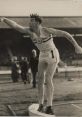 John Savidge, dynamic athlete, preparing for a shot put throw at a historic sporting event, showcasing strength and focus.