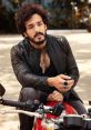 Akhil S poses confidently on a motorcycle, showcasing a stylish leather jacket and distinctive accessories.