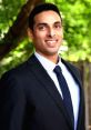 Professional portrait of Suhas M in a suit, smiling outdoors with greenery in the background, conveying confidence and approachability.