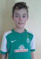 Young boy wearing a green Werder Bremen jersey, smiling confidently, showcasing team spirit and passion for soccer.