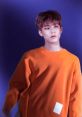 Young man in an orange sweater posing against a purple background, showcasing a stylish and modern look.