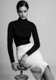 Evelyn Yanez poses confidently in a black turtleneck and sleek white skirt, showcasing modern fashion elegance.