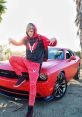 Logan Challenger in vibrant red wrap, featuring a stylish outfit, posing confidently beside the custom muscle car.