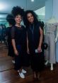 Lilian Silva and friend posing in fashionable black outfits, showcasing chic style in a vibrant mirror-lined room.