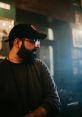 Massimiliano Russo in a cozy setting, wearing a cap and glasses, exuding a thoughtful demeanor amidst ambient lighting.