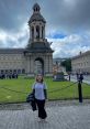 Siena Cohen posing happily in front of a historic building with a tower on a cloudy day, showcasing vibrant campus life.